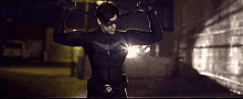 a man in a superhero costume is flexing his muscles in a dark alleyway at night .