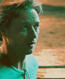 a close up of a man 's face with a turquoise shirt on .