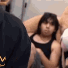 a woman in a black tank top is laying on a couch with a man standing behind her .