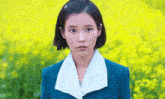 a woman wearing a blue jacket and white collar is standing in front of a field of yellow flowers