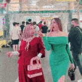 a woman in a green dress is standing next to another woman in a red dress