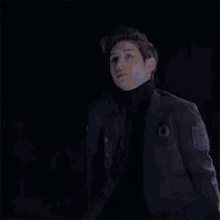 a young man in a suit and turtleneck is standing in the dark .