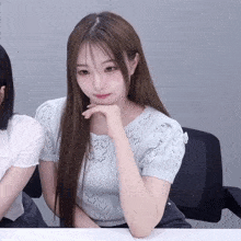 a girl with long hair is sitting at a table with her hand under her chin