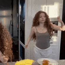a woman in a grey tank top is dancing in front of a plate of food