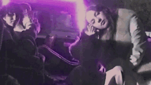 a group of people are sitting in a dark room with a purple light behind them