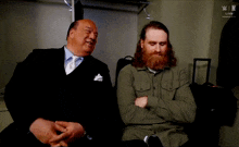 a man with a beard is sitting next to another man in a locker room