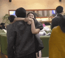 a man in a black jacket is hugging a woman in a crowded room