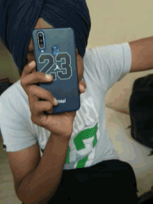 a man wearing a turban is holding a cell phone with the number 23 on the back