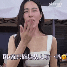 a woman in a white tank top is blowing a kiss in a foreign language