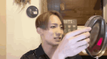 a man is looking at his face in a mirror with a sign that says hots in the background