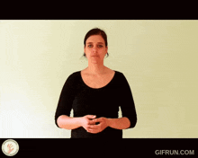 a woman in a black shirt stands in front of a green wall with a gifrun.com logo on the bottom right