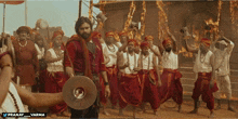a man holding a megaphone stands in front of a group of people wearing red pants