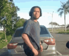 a man in a purple shirt stands in front of a silver car