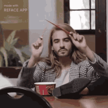 a man with long hair and a beard is sitting at a table with a cup of ramen in front of him