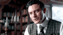 a man in a vest and tie is smiling in front of a bookshelf .