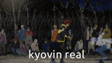 a group of people are gathered around a fence with the words " kyovin real " on the bottom right