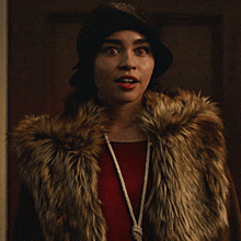 a woman wearing a fur coat and a hat looks at the camera