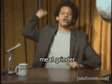 a man in a suit is standing in front of a microphone and saying meat grinder