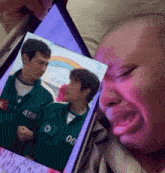 a person is crying while looking at a picture of two people with 456 on their jackets