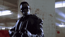 a man in a leather jacket and sunglasses is holding a sword in a dark room .