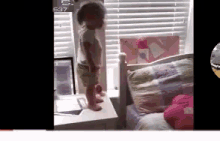 a little girl is standing on a table next to a bed