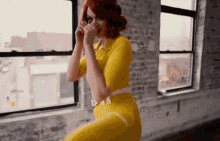 a woman in a yellow outfit is standing in front of a window .