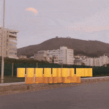 a row of yellow blocks on a sidewalk with buildings in the background and a mountain in the background