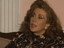 a woman sitting on a couch wearing a black and gold top and gold earrings
