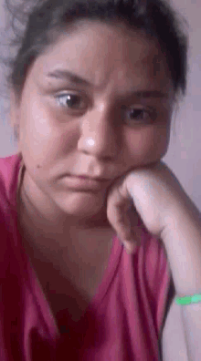 a woman in a pink shirt is making a sad face with her hand on her face .