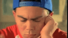 a man wearing a blue hat and a red shirt is holding his head .
