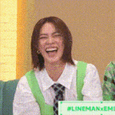 a woman in a green vest and tie is laughing while sitting in front of a sign that says linemanxemi .