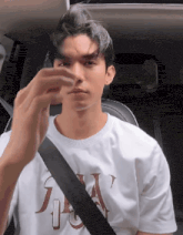 a young man wearing a white t-shirt with the letter j on it is sitting in a car .