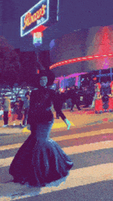 a woman in a black dress is crossing a street in front of a sign that says ' rick 's '