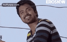 a man in a striped shirt is smiling while standing next to a wire .