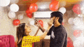 a man and a woman are standing next to each other in a room filled with balloons .