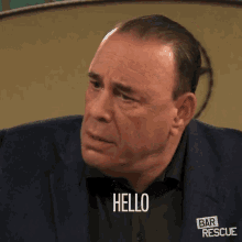 a man wearing a blue suit and black shirt says hello