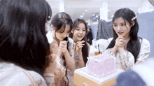 three girls are looking at a pink cake