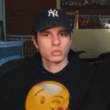 a man wearing a ny hat and a black hoodie with an emoji on it