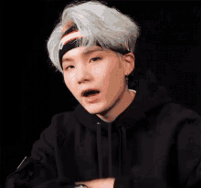 a young man wearing a headband and a black hoodie is making a funny face .