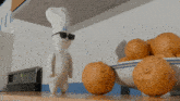 a pillsbury dough boy wearing sunglasses and a chef 's hat stands next to a bowl of oranges