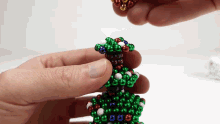 a person is holding a christmas tree made of green red and blue beads