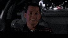 a man in a black and orange shirt is driving a car at night