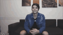 a young man in a blue jacket is sitting on a couch .