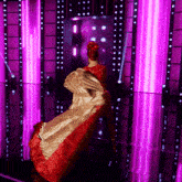 a woman in a red and gold dress is standing in front of a wall of purple lights