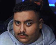 a man with a mustache is wearing a grey hoodie and looking at the camera