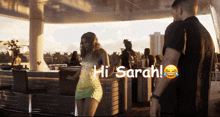 a woman in a green dress says hi sarah in front of a bar