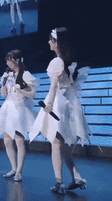 a woman in a white dress is holding a microphone while standing next to another woman in a white dress .