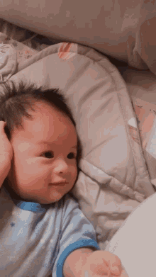 a baby in a blue shirt is laying on a bed looking at the camera