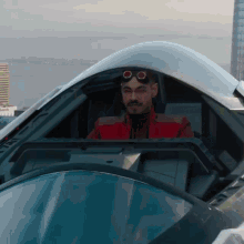 a man in a red jacket and goggles is sitting in the cockpit of a car