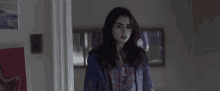 a woman in a plaid shirt and denim jacket is standing in a room .